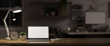 Laptop white screen mockup, alarm clock, stationery, decor plant and table lamp on wood tabletop in modern dark office room at night. close-up image. 3d render, 3d illustration