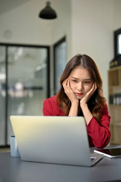 Portrait, Unhappy and bored young Asian businesswoman sits at her office desk looking at laptop screen, feeling tired from work, no work passion.