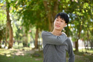 Handsome and happy young Asian man in casual clothes relaxing in the beautiful greenery park on the weekend.