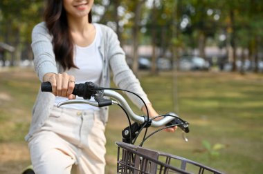 cropped shot of a beautiful and joyful young Asian woman in casual clothes riding a bicycle at the beautiful nature park.