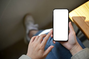 A female using her phone while relaxing in the coffee shop, close-up smartphone white screen mockup. top view
