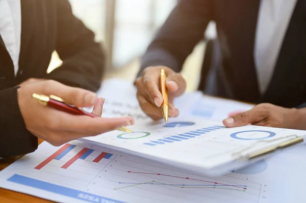 Two professional financial analysts or accountant reviewing financial graphs on the report together, analyzing sales data graph. cropped and close-up hand image