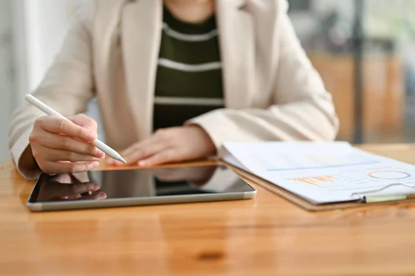 A professional female accountant or financial analyst using digital tablet, working on her business tasks at her desk. cropped and close-up image
