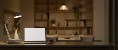 Workspace with laptop white screen mockup, table lamp and decor on tabletop over blurred background of modern contemporary home dining room at night with dining table. 3d render, 3d illustration