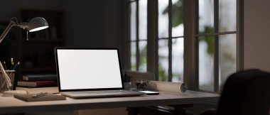 close-up image, Workspace with laptop white screen mockup, table lamp, stationery, and decor on table in modern dark office. 3d render, 3d illustration