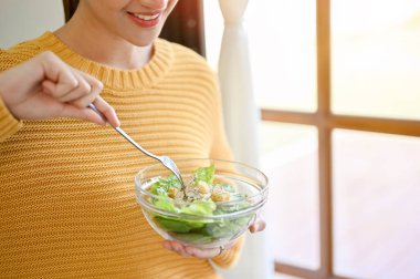 cropped and close-up image, Beautiful woman holding a salad bowl, holding fork, enjoys eating healthy salad mix.