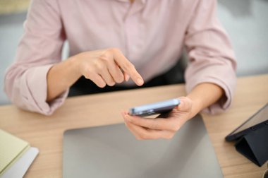 Top view of a female office worker using a smartphone at her desk, using mobile application, sending message to someone, searching something on internet.