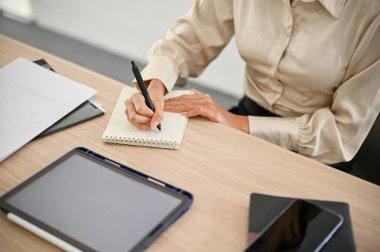 Top view of a professional Asian businesswoman taking notes or making list on her notepad at her office desk.