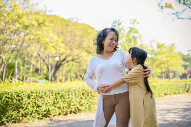 Happy and joyful Asian grandmother and granddaughter showing love, hugging, having a great time together in the city park.
