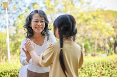 Happy Asian grandmother and granddaughter having fun together, playing fun games, spending the weekend together in the park.