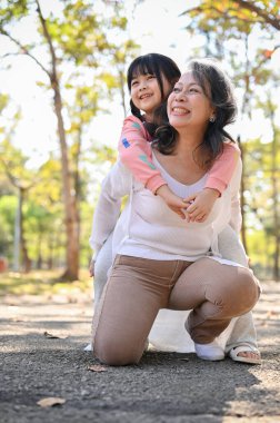 Lovely Asian grandmother and her granddaughter playing in the park together, carrying her little girl, piggy back, having fun time together.
