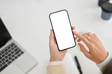 close-up image of a businesswoman using her smartphone at her desk, sending email, texting someone, using mobile application. smartphone white screen mockup.