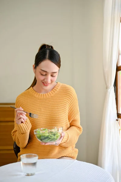 Portrait, A beautiful Asian woman is on diet, enjoys eating salad vegetables mix for her breakfast in her dining room. healthy lifestyle concept