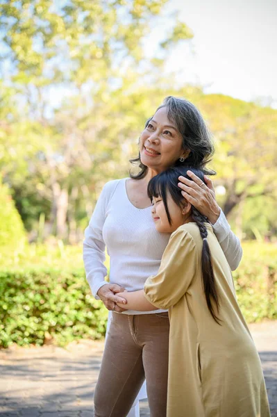 Portrait, Happy Asian grandmother and lovely little granddaughter giving hug to each other, enjoy walking in the park in sunny morning day together.