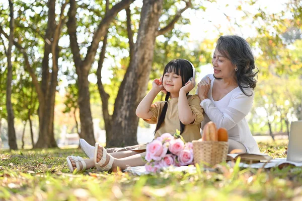 Happy and kind Asian grandmother picnicking with her lovely granddaughter in the park, having happy family time on the weekend together. leisure and family concept