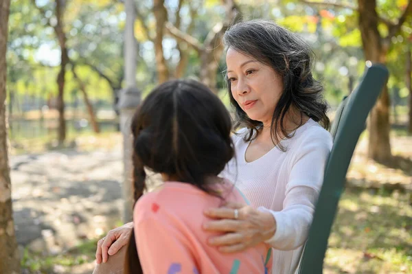 Happy and kind Asian grandmother telling a story to her granddaughter while relaxing in the park together. happy family time concept