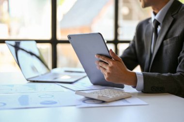 cropped image of professional and smart millennial Asian businessman or male CEO in formal business suit sits at his desk with a digital tablet.