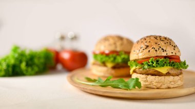 Close-up image of delicious beef burgers on wooden plate on white table with fresh vegetables and seasoning bottles. fast food concept