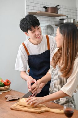 Happy Asian couple having romantic time while cooking, preparing dinner in the kitchen together for their dinner night.