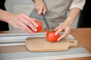 Close-up image of lovely couple preparing salad's ingredients together, cutting tomatoes on chopping board.