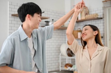 Loving and playful Asian couple dancing in the kitchen, smiling, having happy and romantic moment while preparing breakfast. healthy and happy relationship
