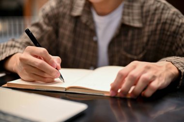 Cropped shot of a male college student doing homework, writing or taking notes on his book, sitting in the coffee shop.