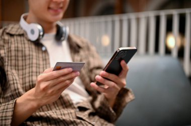 Close-up image of an Asian man using credit card payment service on online shopping app, holding a credit card and his phone. mobile banking, money transferring