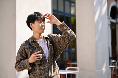 Handsome young Asian man in trendy outfit strolling around the city square, enjoys his summer vacation.