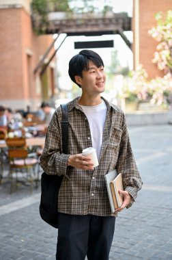 Portrait of handsome and happy young Asian man in trendy casual outfit walking in the city square.