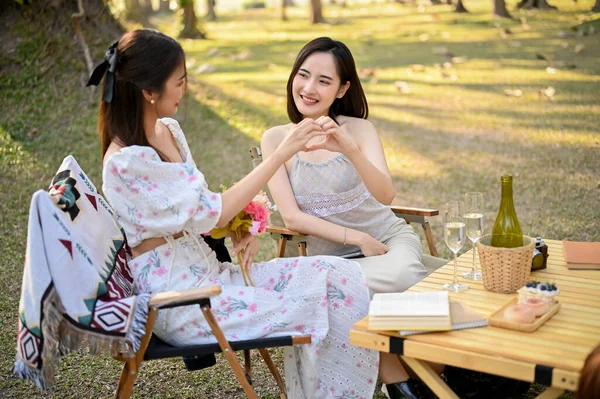 Çekici ve çekici Asyalı kadın parkta piknik yaparken arkadaşıyla el işareti yapıyor. Arkadaşlık, en iyi arkadaş, kadın çift, el hareketi