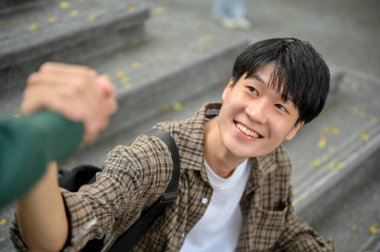 Close-up image of smiling and happy young Asian male college student giving friendly handshake with his friend. friendship, classmate, buddy, best friend.