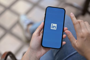 Chiang Mai, Thailand - Feb 6 2023: Top view of a female hands holding a smartphone with LinkedIn logo on screen, iPhone with LinkedIn application logo.