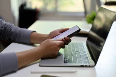 Side view of a businesswoman using her smartphone at her office desk. text, message, chat, communication, social media, mobile application