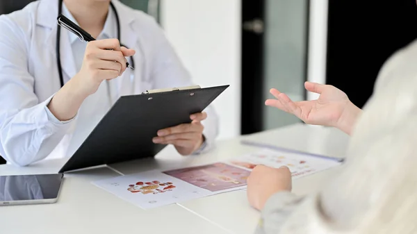 Professional female doctor meeting with her patient in the doctor\'s office, discussing treatment plans and dispensing a medical prescription. cropped image