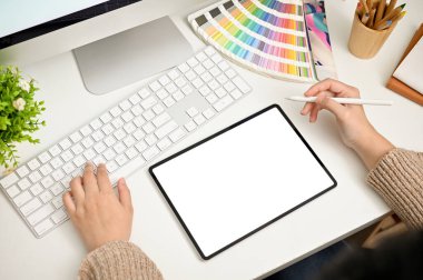 Top view of a professional female graphic designer or freelance editor working at her modern desk, using laptop and digital tablet. tablet white screen mockup