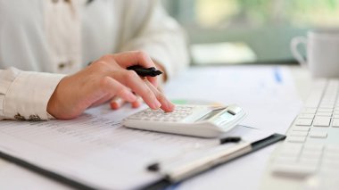 Close-up image of a businesswoman or female accountant using calculator, working on financial report at her desk.