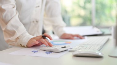 A professional businesswoman or female accountant using calculator, calculating monthly sales, working on financial report at her desk.
