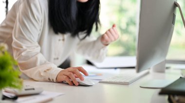 Cheerful Asian businesswoman showing clenched fist, checking email on computer and celebrating her success at office desk. cropped image