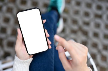 Top view of a woman using her smartphone at the backyard, smartphone white screen mockup.