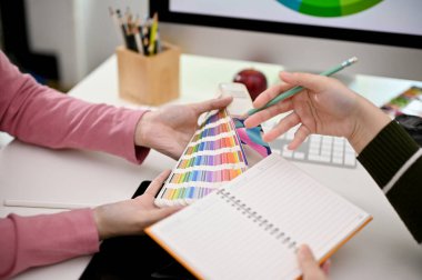 Close-up image of two graphic designers designing their new product together in the office, choosing color template from color chart.