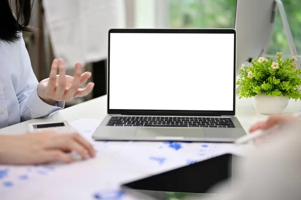 Laptop white screen mockup on a meeting table, businesspeople are in the meeting, discussing and planning business investment plan. cropped image