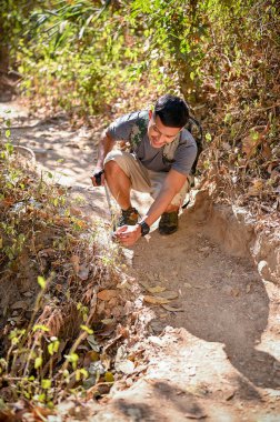 Handsome Asian man with trekking gear trekking at the rocky mountain trail on sunny day. outdoor activity and lifestyle concept