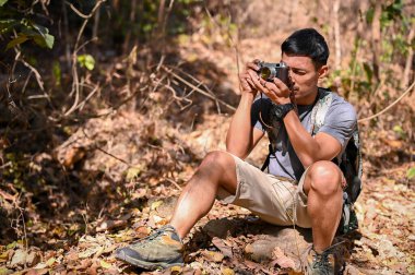 Handsome and active Asian man in active outfit taking a picture with film camera while hiking at the mountain trail. outdoor activity and sport concept