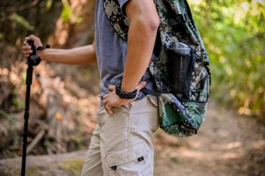 Cropped image of an active Asian male traveler with backpack and trekking gear stands in the forest, trekking or hiking alone.