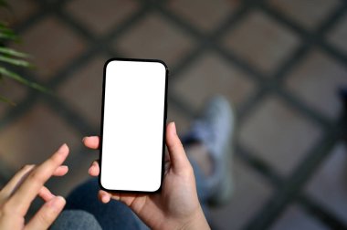 Close-up image of a woman's hand holding a smartphone white screen mockup for display your graphic banner on screen over blurred background.