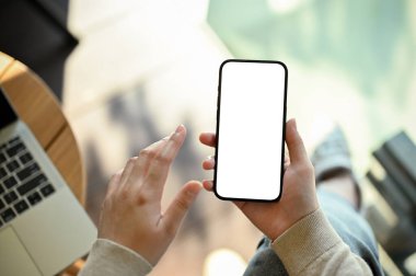 A woman remote working at the cafe, using her smartphone to contact someone, using mobile application, checking mail box on her phone. phone white screen mockup, close-up image