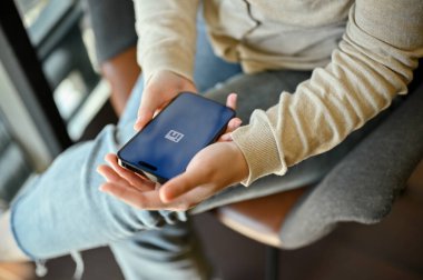 Chiang Mai, Tayland - 14 Şubat 2023: Günlük giysiler içindeki bir kadının üst görünümü kahve dükkanındaki masada oturuyor, akıllı telefonunda LinkedIn uygulaması kullanıyor. Ekranda LinkedIn logosu olan bir akıllı telefon