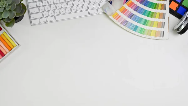 Top view of a minimal white graphic designer\'s desk with accessories and copy space. computer keyboard, color palette chart, color checker.