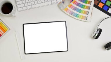 Top view of a modern minimal white graphic designer office desk with keyboard, headphones, color palette, color checker, stylus pen and digital tablet white screen mockup.