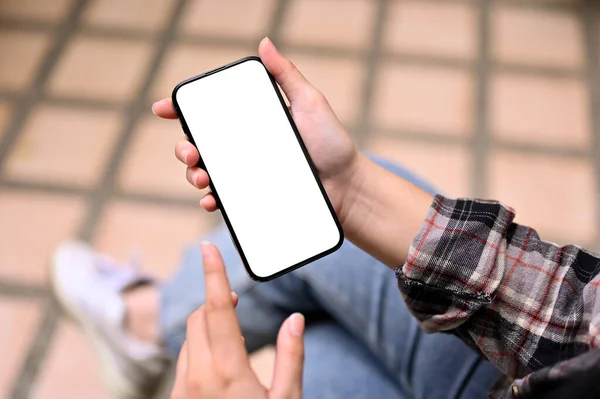 Close-up image of a woman in flannel shirt and jeans relaxing in the backyard and using her smartphone. smartphone white screen mockup
